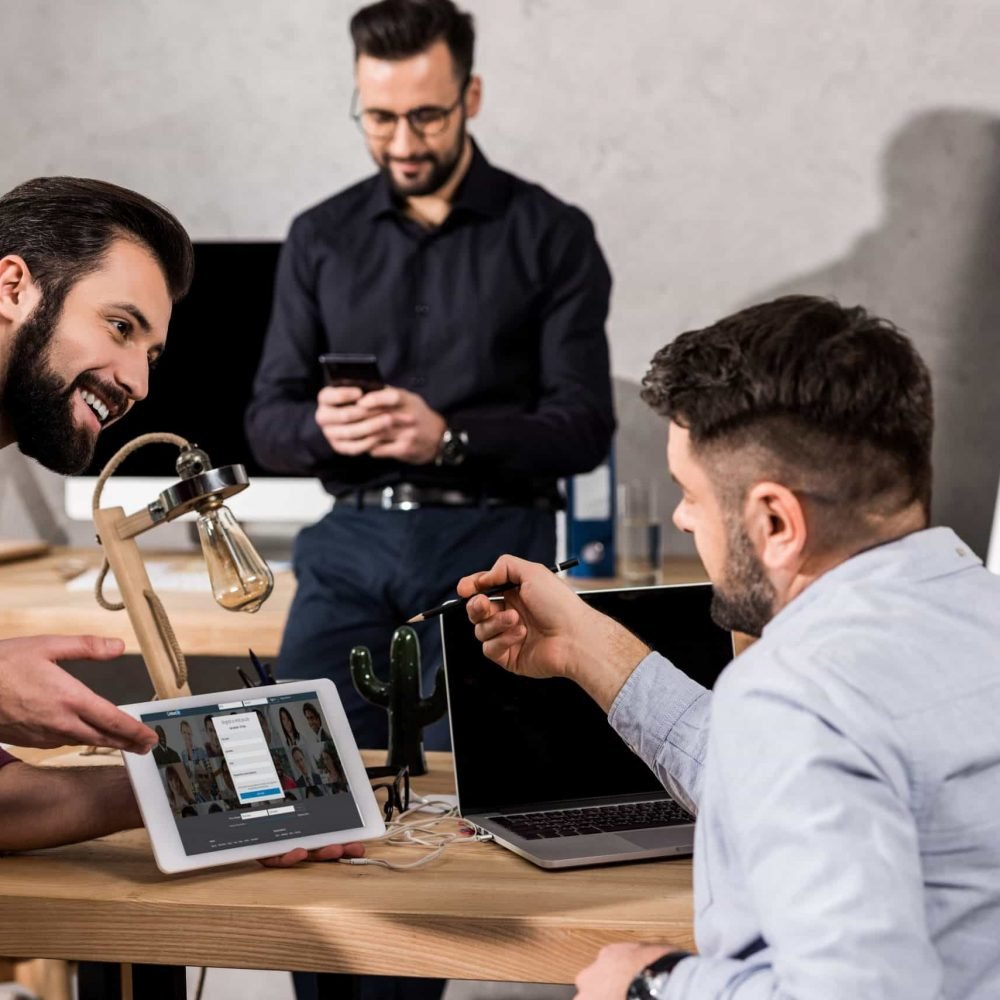 smiling businessman showing colleagues linkedin page on tablet